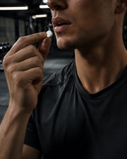 Person holding a white supplement capsule in a gym setting